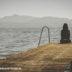 Allein auf einem Steg am Wasser – Natursitzen in stiller Verbindung mit See, Bergen und Himmel