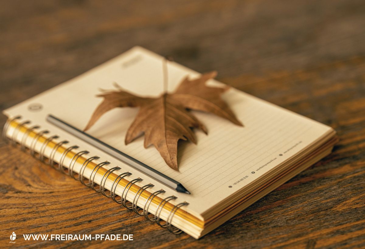 Spiralgebundenes Notizbuch mit getrocknetem Blatt auf Holztisch – Symbolbild für Journaling in der Natur