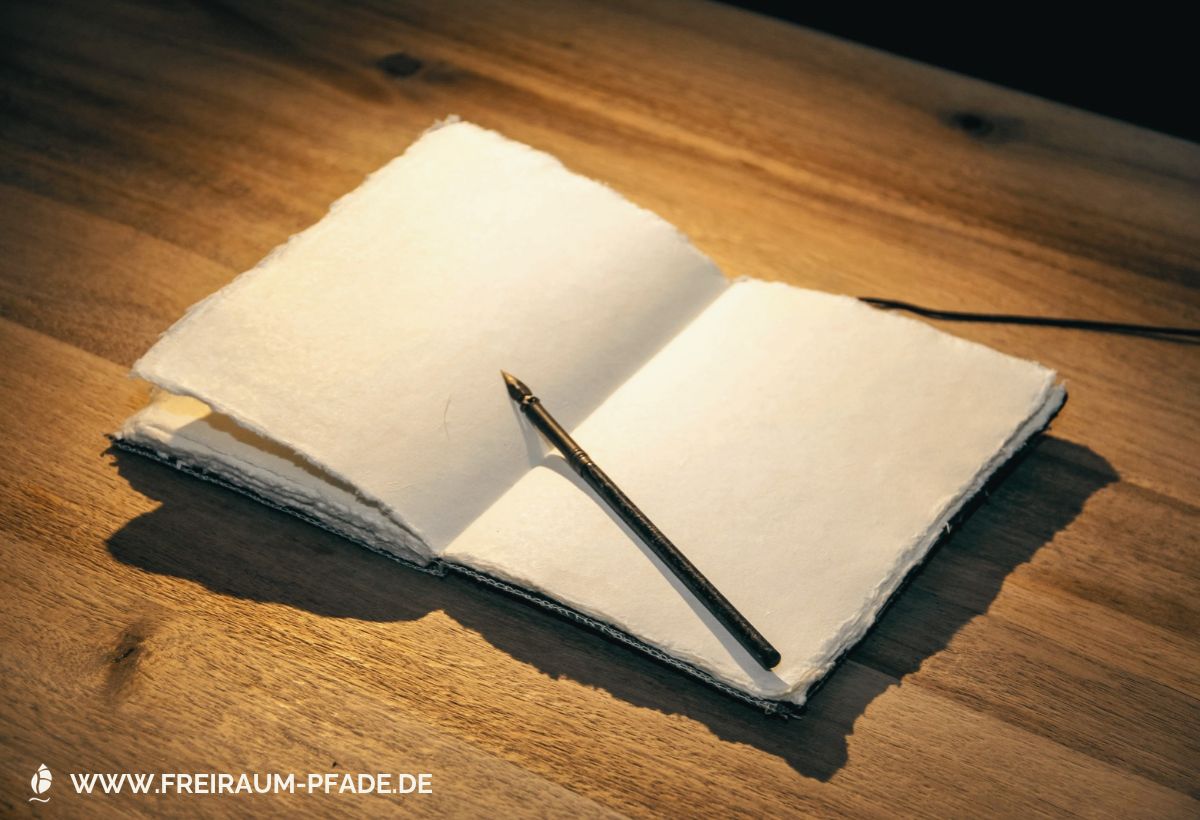 Leere Seiten eines cremefarbenen Notizbuches, auf denen auch ein dunkelbrauner Stift liegt. Das Buch liegt auf einem dunkelbraun gemaserten Holztisch.